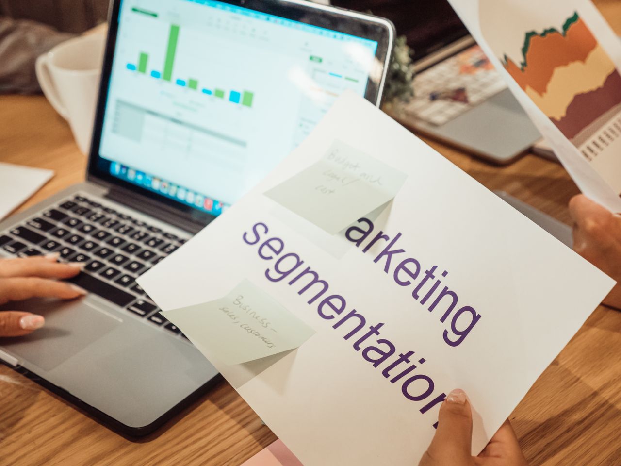 A contemporary workspace where hands review marketing data on a laptop and printed documents.